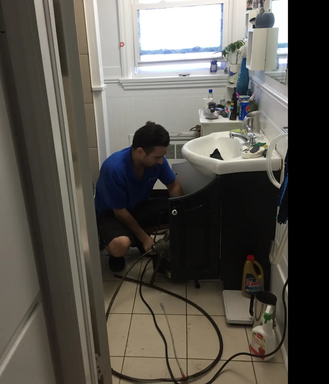 Plumber running a drain machine at a sink cabinet